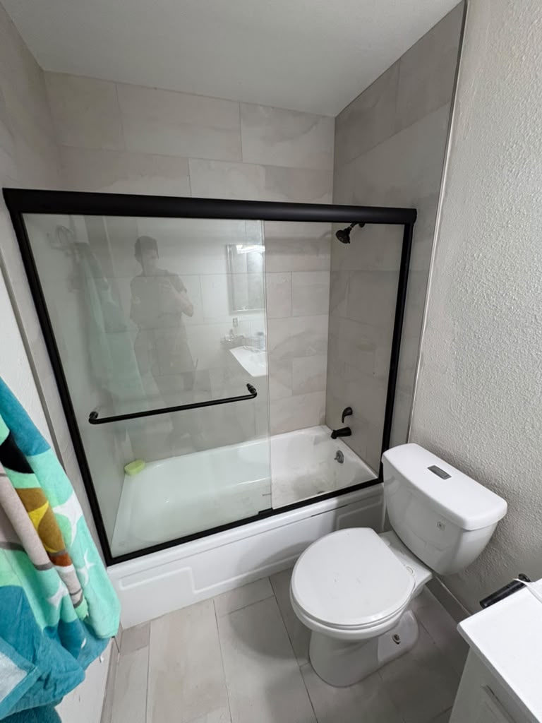 After — finished tub and shower with tile surround, new glass door and black fixtures